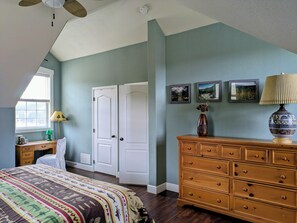 Un dormitorio con una cama grande, un tocador, una ventana con persianas y un ventilador de techo.