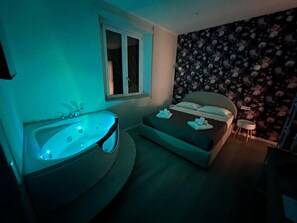 A bedroom with a large bathtub, a window, and a floral wallpaper. - Aurelia Garden Rooms B&B (Rome)