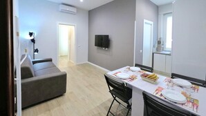 Een moderne woonkamer met een grijze bank, een eettafel gedekt voor vier personen en een flatscreen televisie aan de wand.