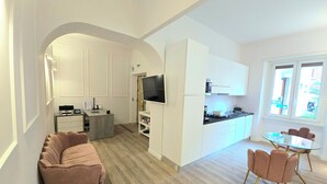 Een moderne keuken met witte kastjes, een ingebouwde televisie en een eethoek met een glazen tafel en roze stoelen.