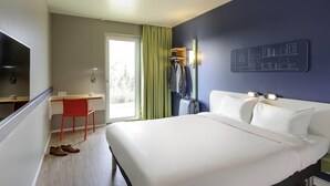 A hotel room with a bed, a desk, a chair, a television, and a window with curtains. - Ibis Budget Konstanz (Konstanz)