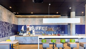 A modern cafe with a bar area, seating with colorful stools, and a counter with coffee-making equipment. - Ibis Budget Konstanz (Konstanz)