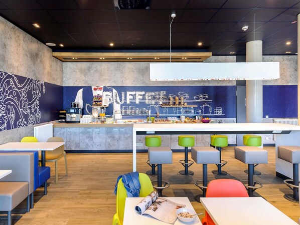A modern cafe with a bar area, seating with colorful stools, and a counter with coffee-making equipment. - Ibis Budget Konstanz (Konstanz)