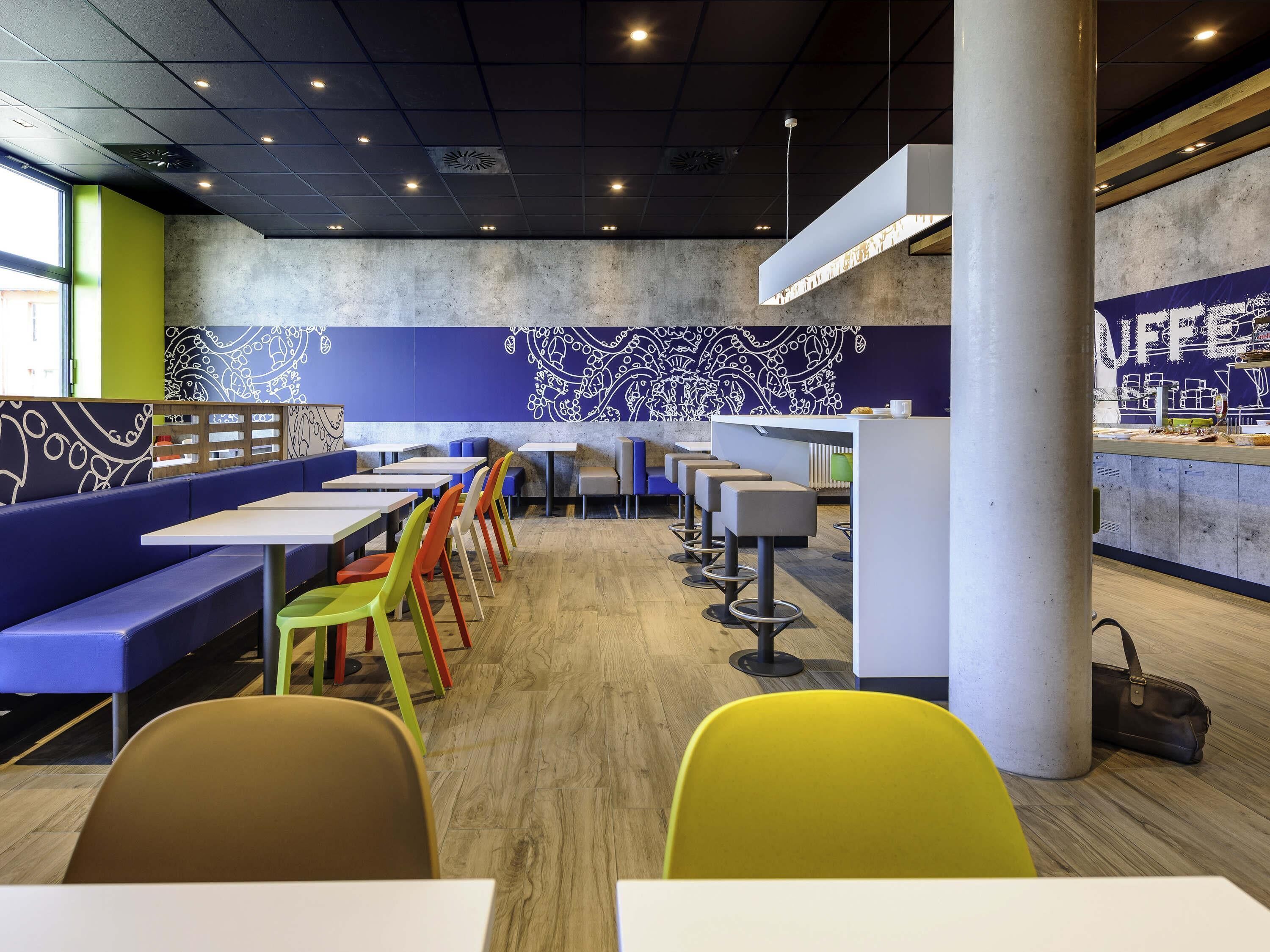 Un interior de restaurante moderno con mesas altas, sillas coloridas y una zona de bar.