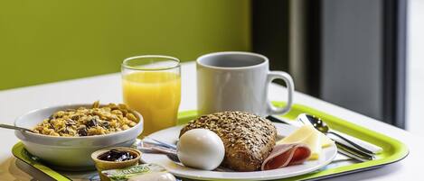 Bandeja de desayuno con cereal, tostadas, huevos, queso y un vaso de jugo de naranja.