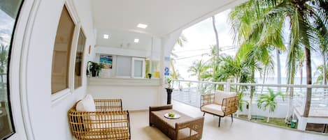 A balcony with wicker furniture, a small table, and a view of palm trees.