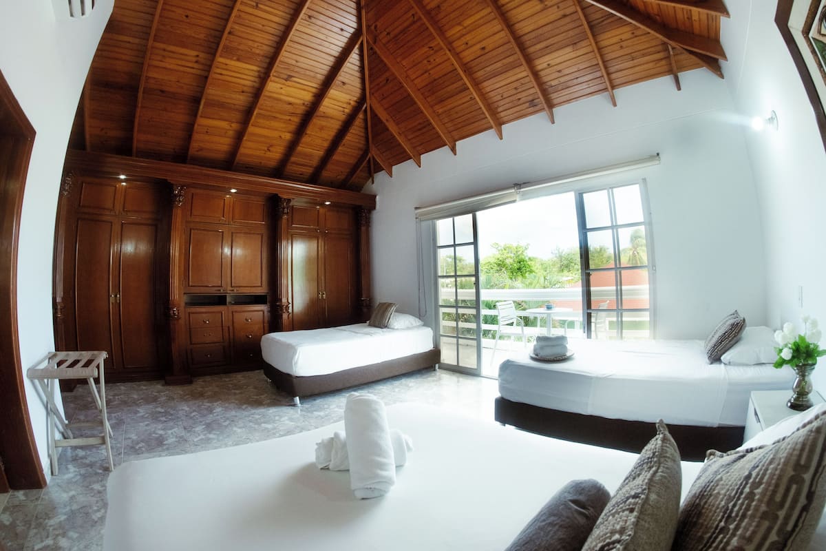 Ein geräumiges Zimmer mit hoher Holzbalkendecke, einem großen Bett, einer Couch und einer Glastür, die zu einem Außenbereich führt.