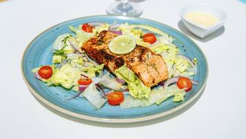 Une assiette de saumon grillé, accompagnée d’une salade et d’un verre de cocktail rose, décoré d’une tranche de citron vert.