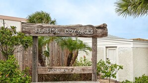 Une pancarte en bois sur laquelle on peut lire « SEASIDE COTTAGES » et « LINDSBEACH.COM », placée devant une clôture et un décor de verdure.