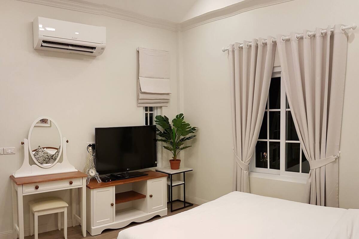 A bedroom with a bed, a desk with a TV, a mirror, and a potted plant.