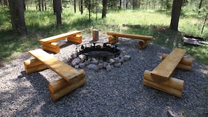 Ein Campingplatz mit Feuerstelle, umgeben von hölzernen Bänken und Baumstämmen.