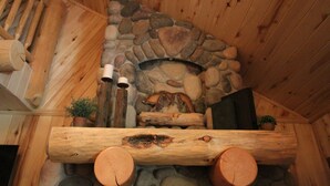 Ein rustikaler Kamin aus Stein mit einer Sitzbank aus Holz, umgeben von Holzscheiten und einer Holzbalkendecke.
