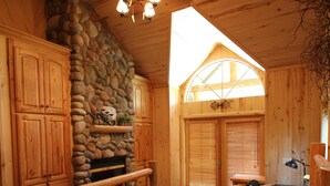Ein Schlafzimmer einer Holzhütte mit Kamin aus Stein, einem Bett mit vielen Kissen und einem Nachttisch mit Lampe.