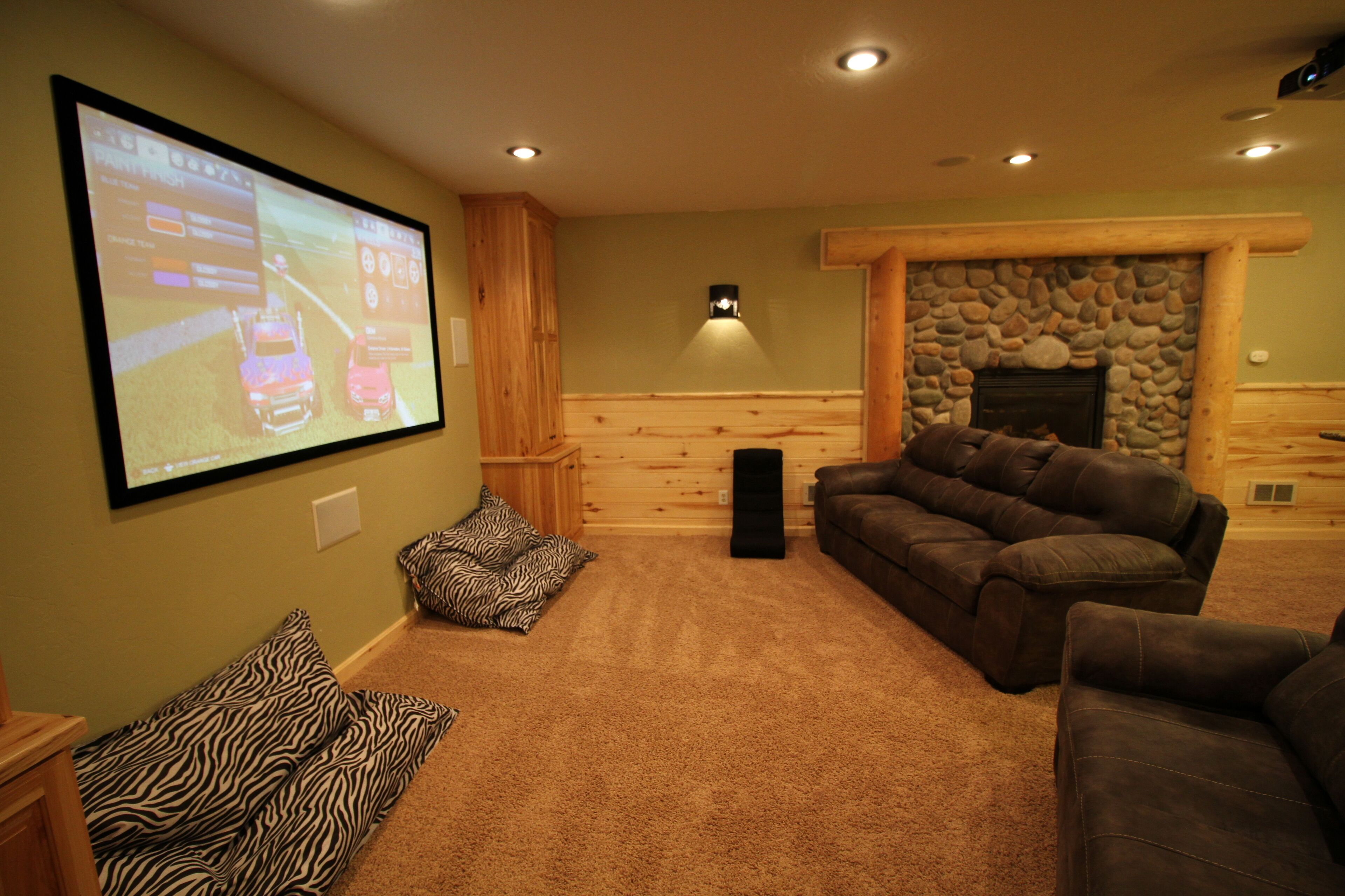 A cozy living room with a large screen, comfortable seating, and a stone fireplace.