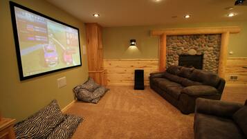 A cozy living room with a large screen, comfortable seating, and a stone fireplace.