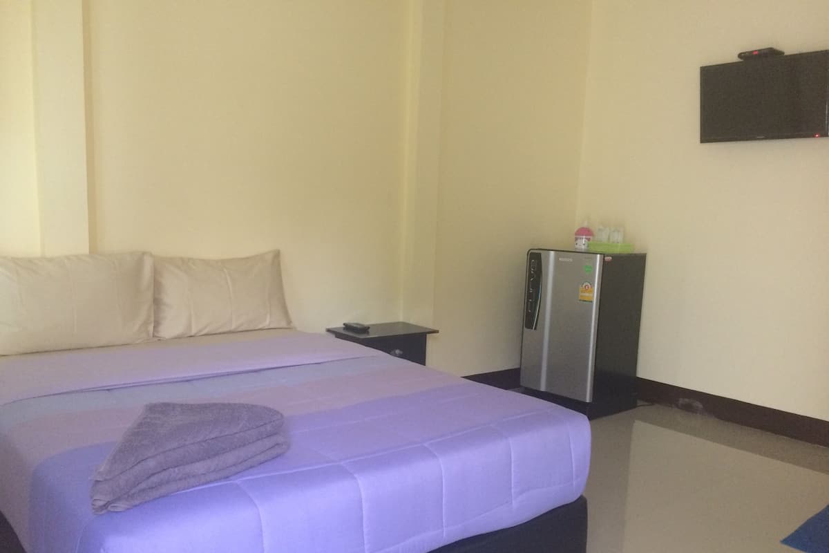A hotel room with a bed, a small table, a refrigerator, and a wall-mounted TV.
