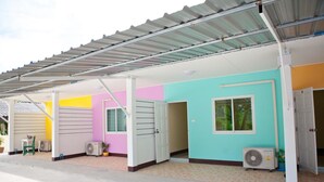 Una hilera de edificios de un solo piso, de colores llamativos, con techo de metal, unidades de aire acondicionado y una entrada sencilla.
