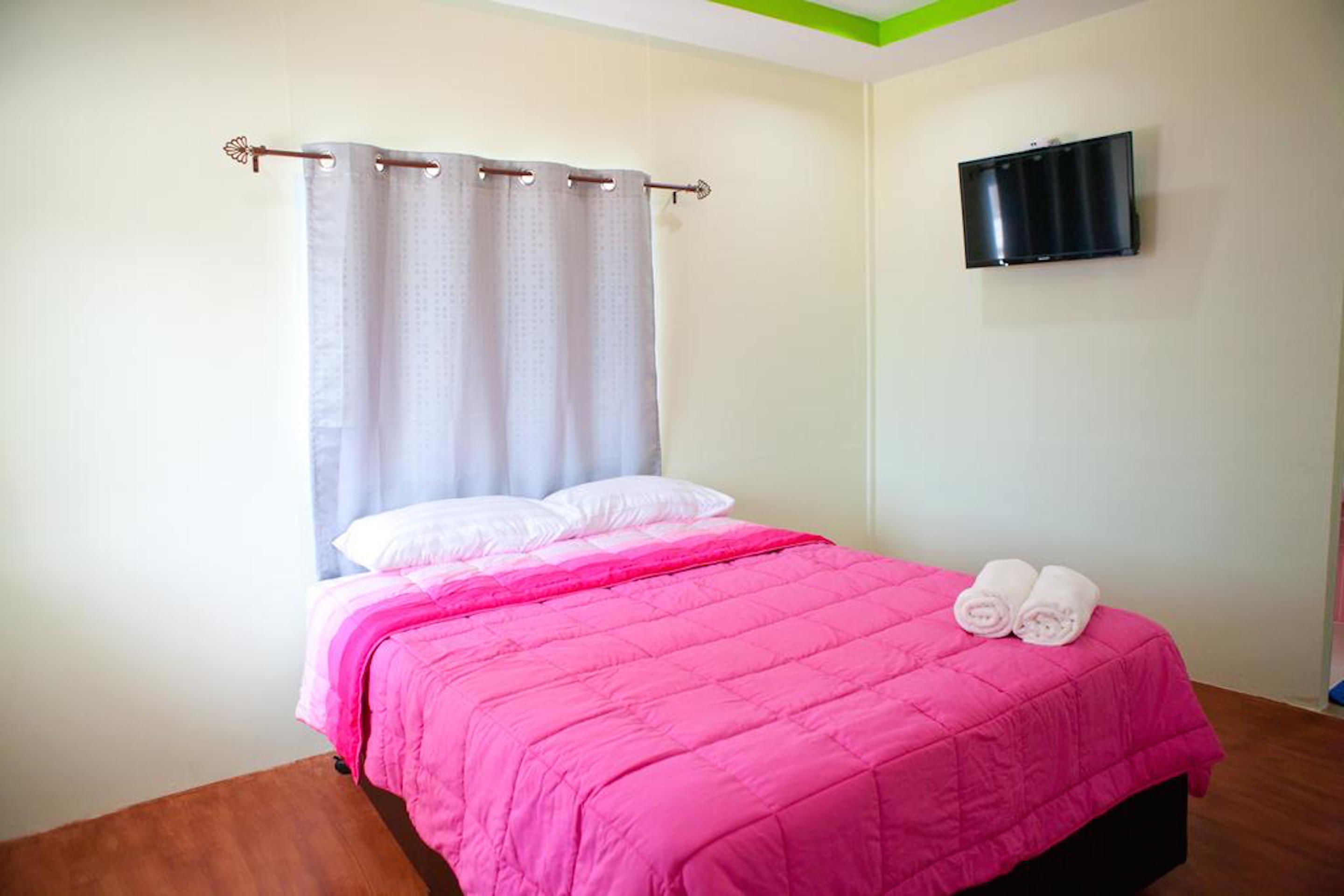 Un dormitorio con una cama, un televisor en la pared y una cortina.