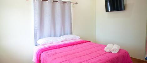 Un dormitorio con una cama, un televisor en la pared y una cortina.