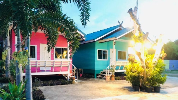 Una casa de dos pisos con fachada rosa y azul, un porche con banca y una pequeña escalera que lleva a la entrada.