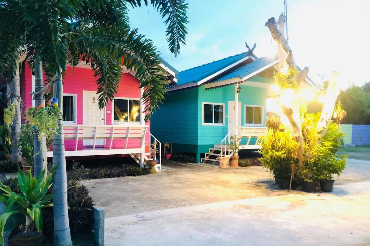 A two-story house with a pink and blue exterior, a porch with a bench, and a small staircase leading to the entrance.