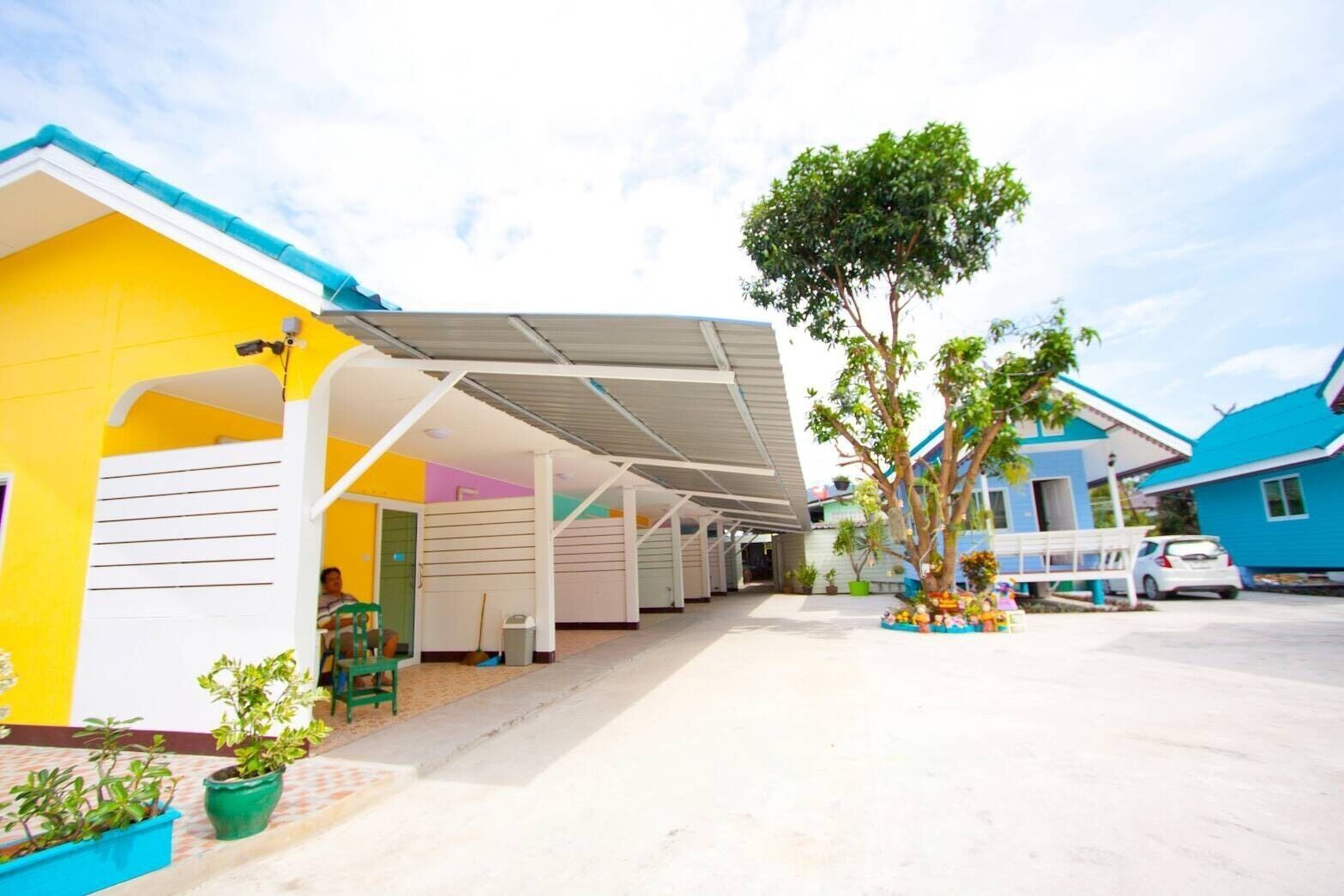 A covered outdoor area with a yellow building, a blue building, and a tree.