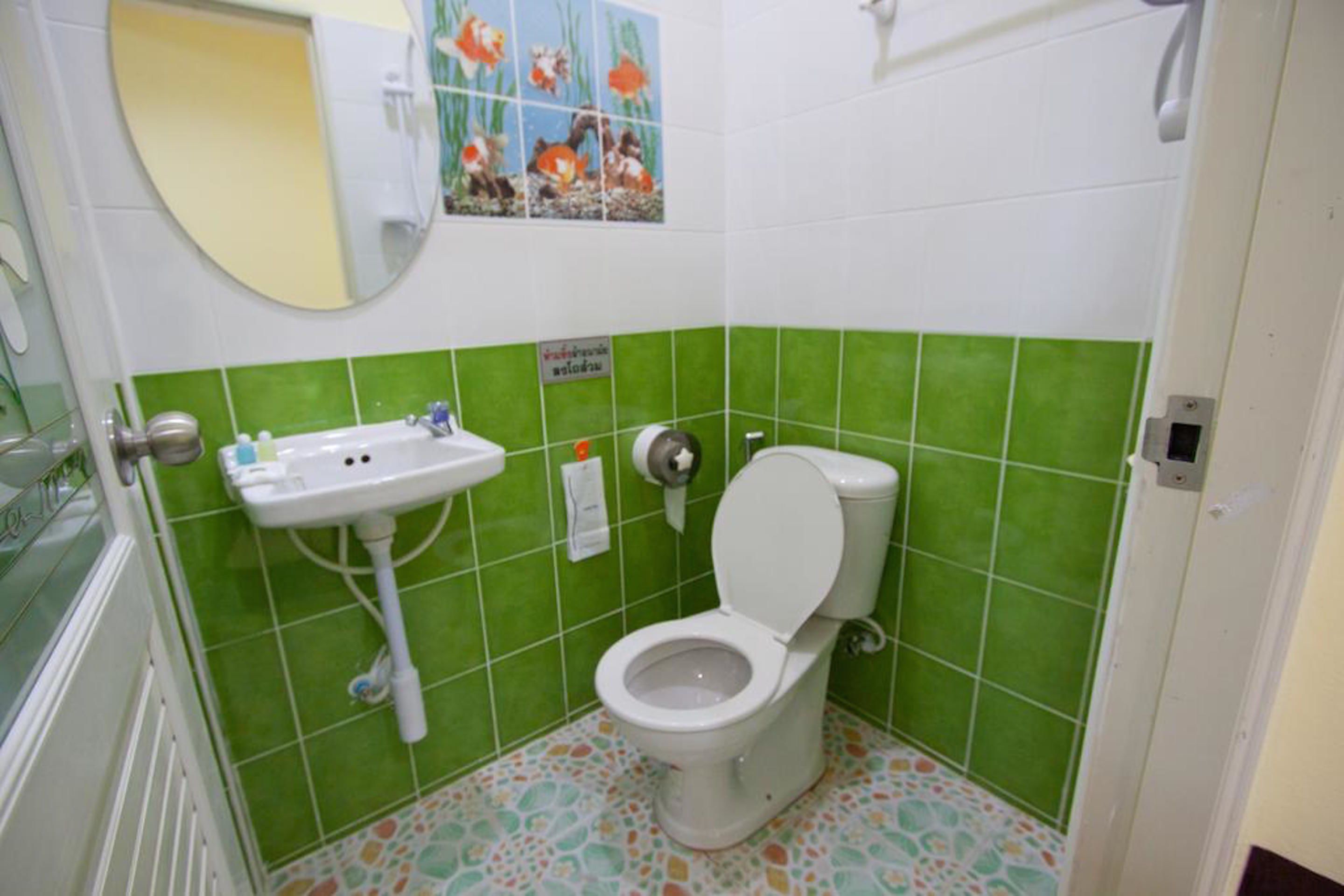 A bathroom with a toilet, sink, and green tiled walls.