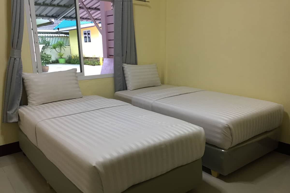 A room with two single beds, a window with curtains, and a view of a building outside.