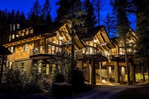 A multi-story log cabin with a balcony and a covered walkway, surrounded by dense forest. - Available NEW YEAR'S WEEK- SLOPESIDE with PRIVATE Treetop Hot Tub-2 Bdm/2 Bath Luxury Ski-in/Ski-out (Whitefish)