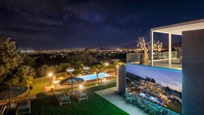 A modern outdoor pool area with lounge chairs, a pergola, and a view of a cityscape at night. - 9 beds, 7 wc, sauna, jacuzzi, pool, cinema, bar, bbq, firepit, helipad, parking (Chania)