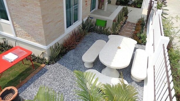 A modern outdoor seating area with a table and chairs, surrounded by gravel and plants. - Sandy Home Sattahip (Sattahip)