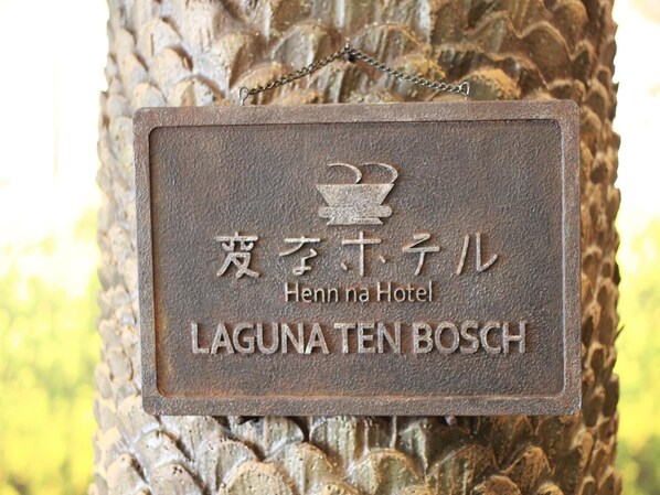 A metal plaque with the text "Henn na Hotel" and "LAGUNATEN BOSCH" on a tree trunk.