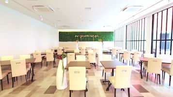 A spacious dining area with multiple tables and chairs, a green wall with plants, and large windows.