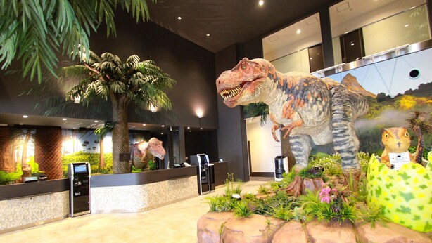 A reception area with a large dinosaur statue, a palm tree, and a small dinosaur figurine.