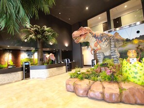 A reception area with a large dinosaur statue, a palm tree, and a small dinosaur figurine.