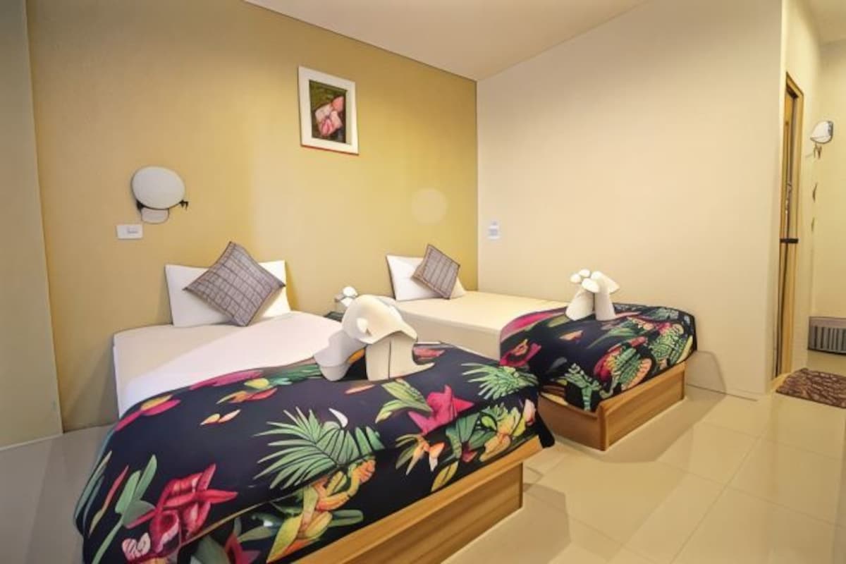 A hotel room with two beds, a small wall-mounted light, a framed picture, and a tiled floor.