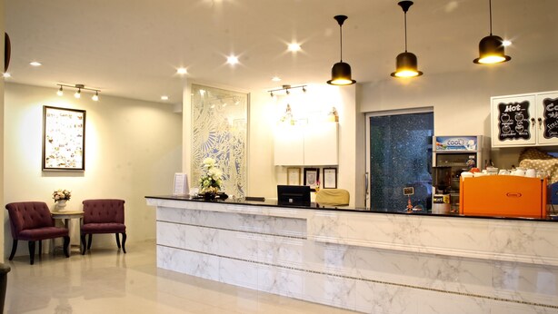 A hotel reception area with a marble counter, two plush armchairs, a coffee machine, and a decorative wall with a framed picture. - Green Apple Villa (Sattahip)