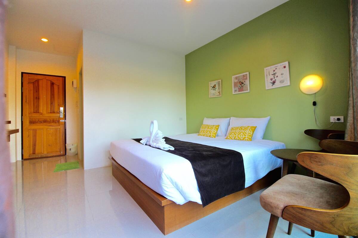 Quarto de hotel com uma cama, uma cadeira e uma luminária fixada na parede.