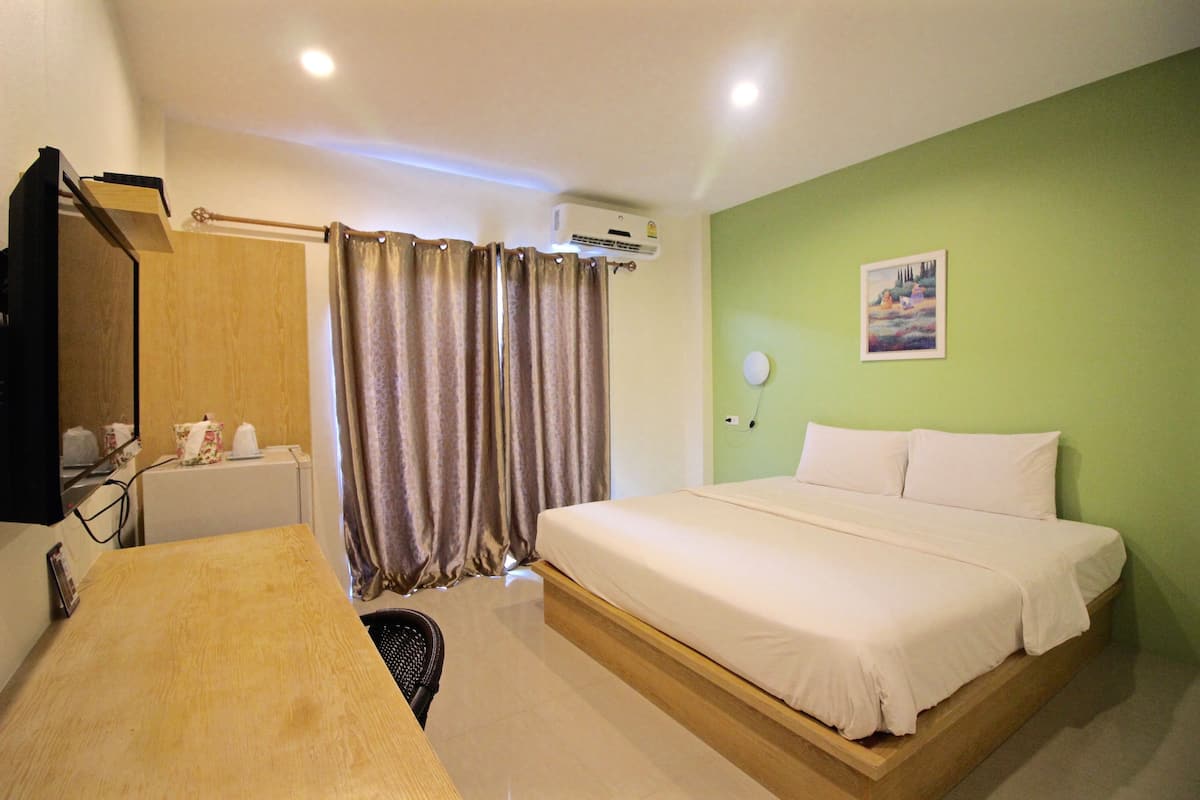 Quarto de hotel com cama, escrivaninha, cadeira, aparelho de ar condicionado, cortina e um quadro na parede.