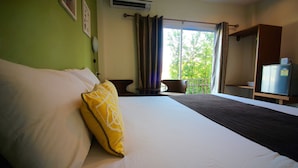 A hotel room with a large bed, a small table, a chair, a balcony with curtains, and a refrigerator. - Green Apple Villa (Sattahip)