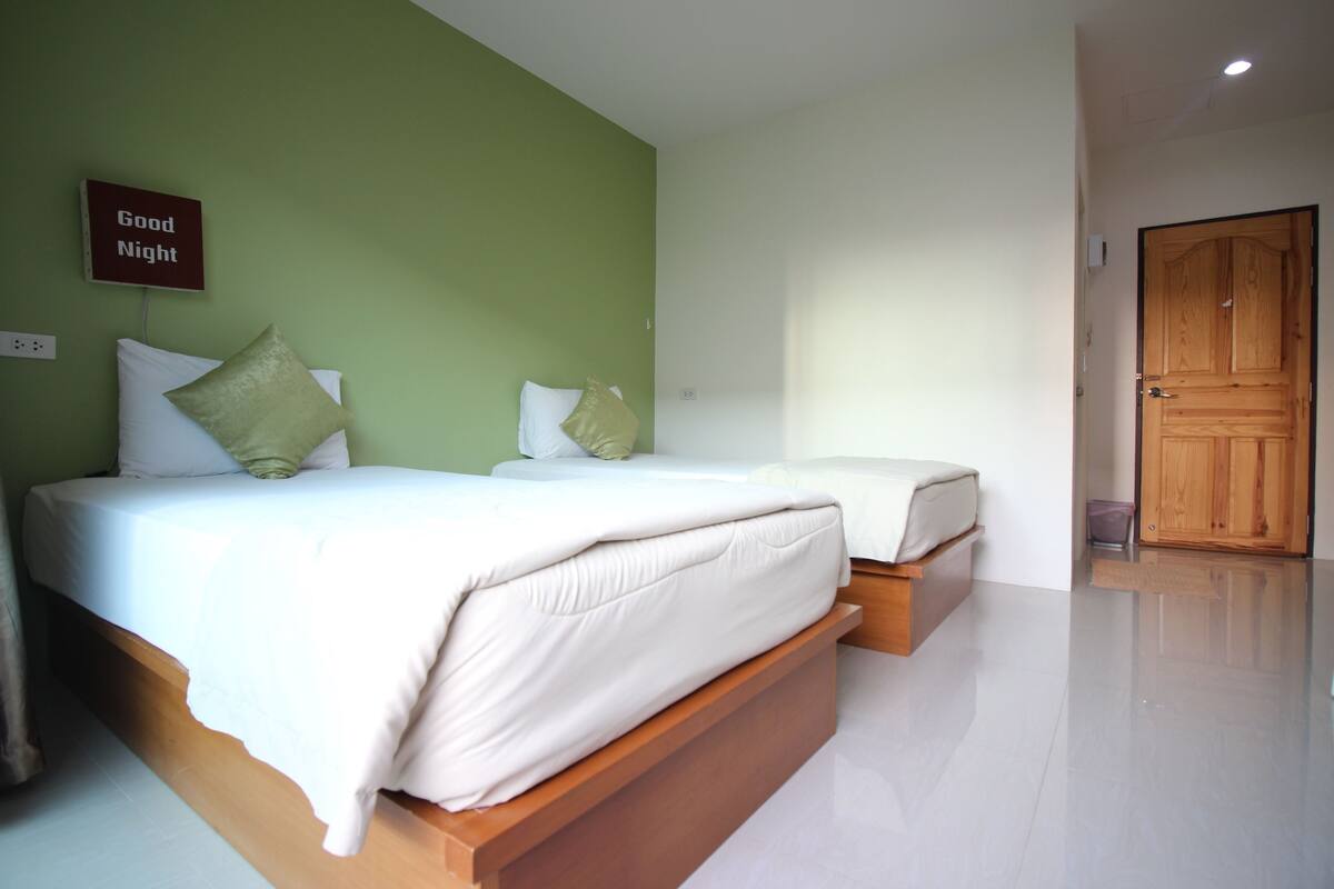 Quarto com duas camas, parede verde e porta de madeira.