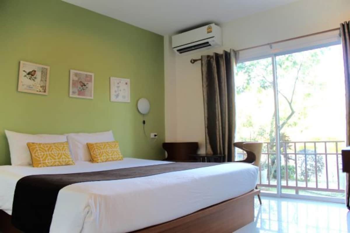 A hotel room with a bed, a window with curtains, an air conditioning unit, and wall art.