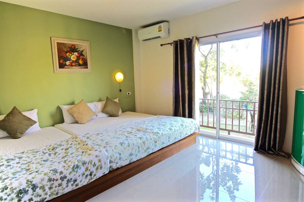 Quarto de hotel com uma cama grande, um quadro na parede, aparelho de ar condicionado e vista para o exterior por uma porta de correr.