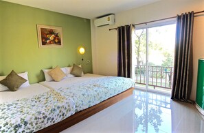Ein Hotelzimmer mit einem großen Bett, einem Gemälde an der Wand, einer Klimaanlage und Blick ins Freie durch eine Schiebetür.