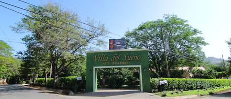 Villa del Sueno Hotel Restaurant entrance with a green archway, surrounded by trees and a clear sky.