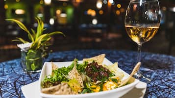 En un plato, una ensalada con una copa de vino blanco sobre una mesa con mantel estampado azul.