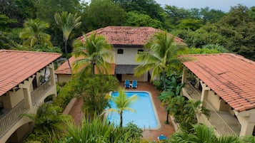 Un resort con una piscina central rodeada de palmeras y un edificio con techo de paja.