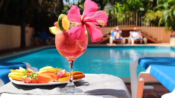 A poolside setting with a drink garnished with fruit and a hibiscus flower, a plate of sliced fruits, and a pool in the background. - Hotel Villa del Sueño (Sardinal)