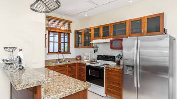 A modern kitchen with granite countertops, wooden cabinets, a stainless steel refrigerator, a microwave, and an oven.