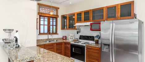 A modern kitchen with granite countertops, wooden cabinets, a stainless steel refrigerator, a microwave, and an oven.